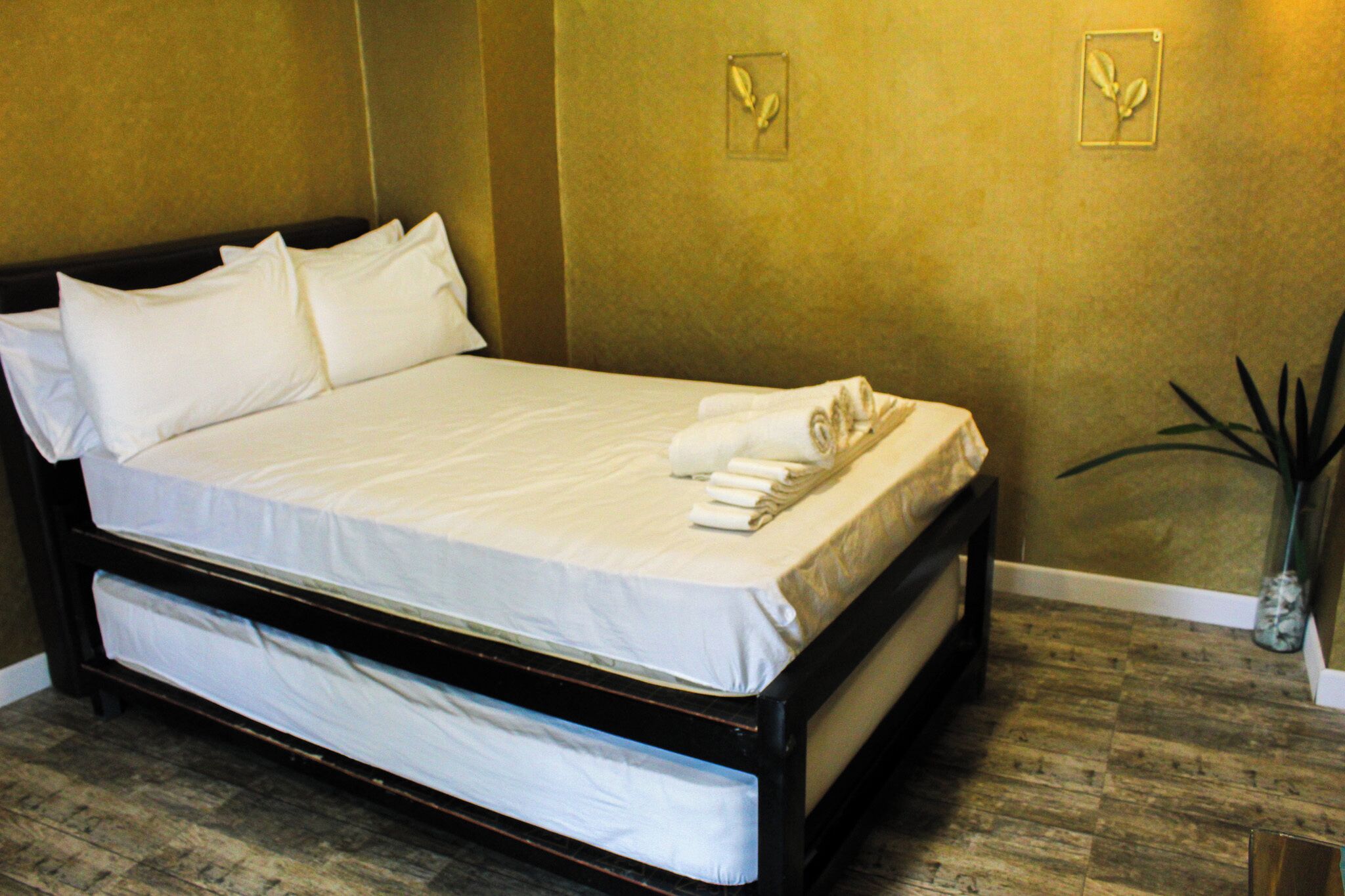 A hotel room with a bed, pillows, a rolled-up towel, and a small potted plant.