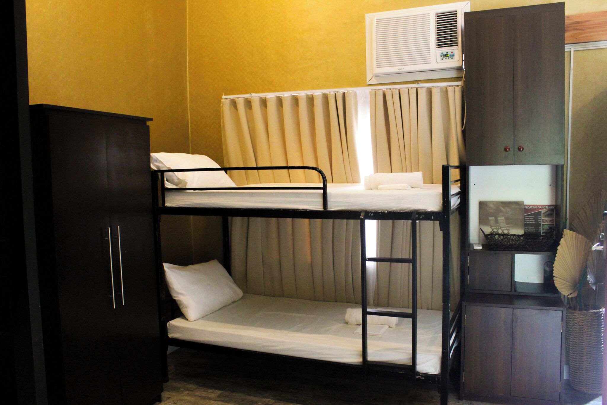 A bunk bed room with a wardrobe, an air conditioning unit, and a small cabinet with a fan.