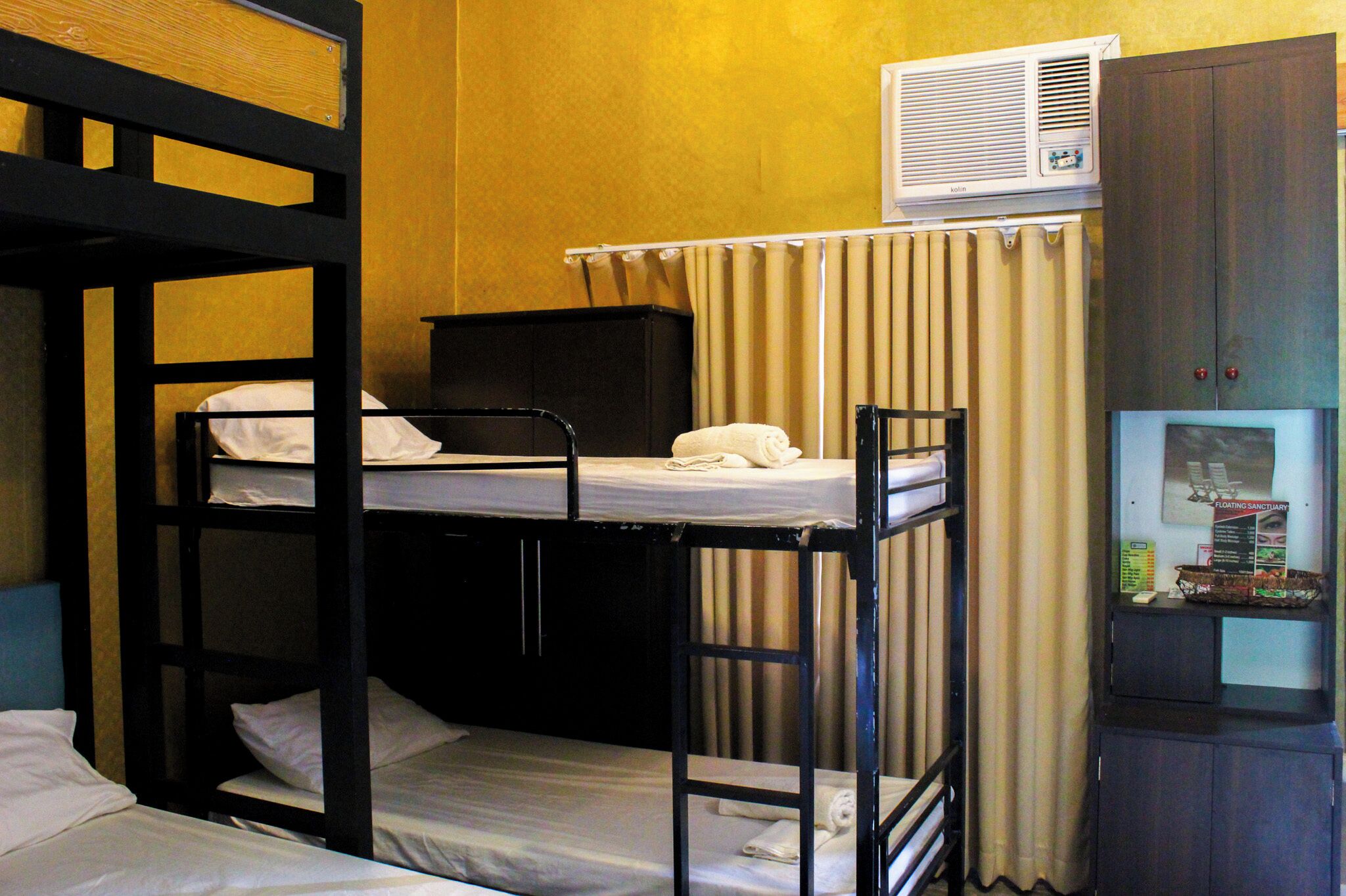 A bunk bed room with a desk, a chair, a window with curtains, and a wall-mounted air conditioner.