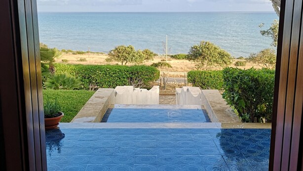 Vista attraverso un arco di una piscina che si apre su una spiaggia.