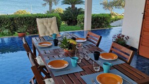 Zona pranzo con vista sul mare, caratterizzata da un tavolo in legno apparecchiato con piatti, bicchieri e un centrotavola con ananas.