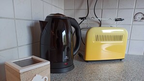 Keittiön työtasolla on musta sähköinen vedenkeitin, keltainen retrotyylinen leivänpaahdin ja puinen rasia, jonka päällä on teekupin kuva.