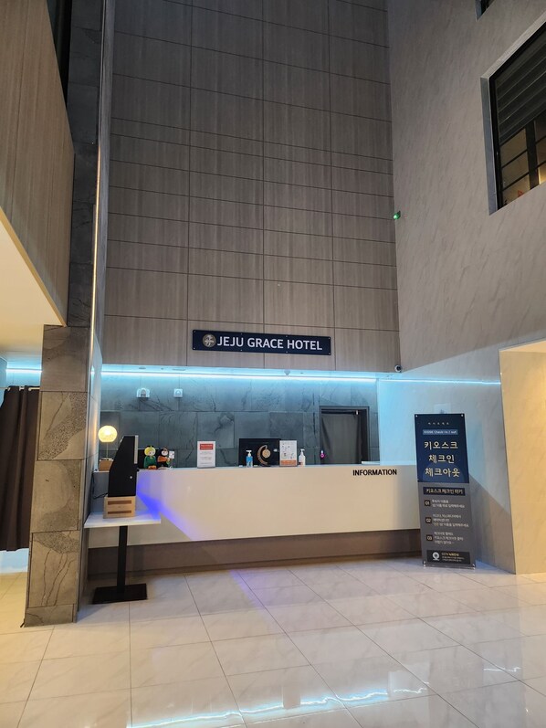 A hotel reception area with a sign for Jeju Grace Hotel, a reception desk, and an information board.