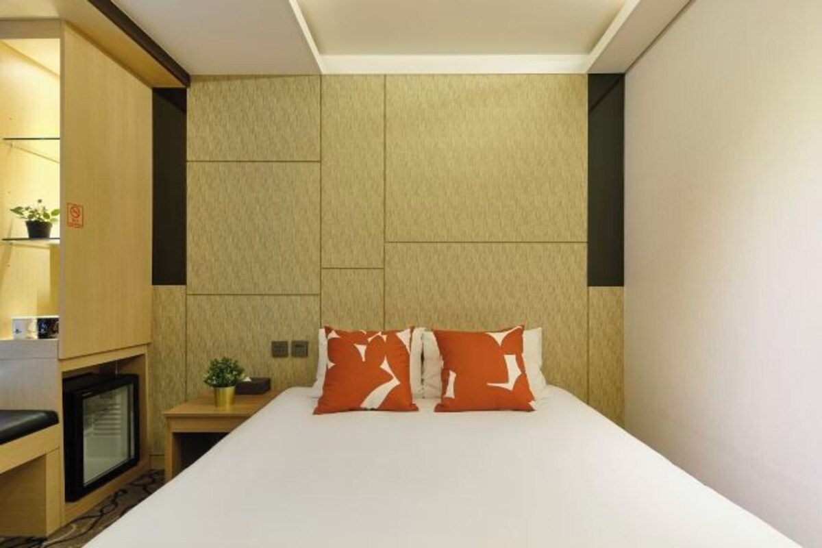 A hotel room with a bed, a small table with a plant, a TV, and a wall-mounted shelf.