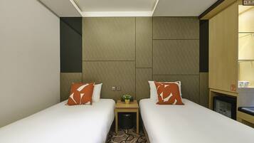 A hotel room with two single beds, a small bedside table with a plant, and a minibar.