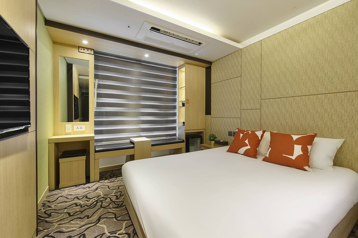 Habitación de hotel con cama, escritorio, espejo y ventana con persianas.