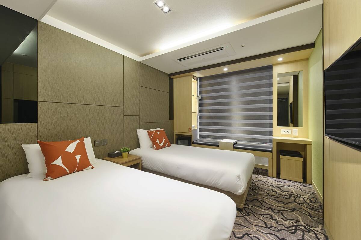 Habitación de hotel con dos camas, un escritorio, un espejo y una ventana con persianas.