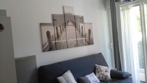 Un salón con un sofá azul, un cuadro abstracto grande y vistas de un jardín a través de una ventana.