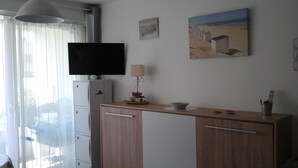 Una habitación con televisión, lámpara, un cuadro y escritorio con cajones.