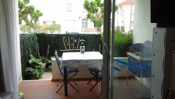 Un patio con mesa y sillas, una parrilla y vistas a un seto y edificios.