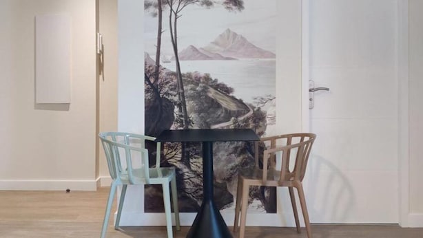 Ein Essbereich mit Tisch und zwei Stühlen, eine Tür mit einem Gemälde und ein Lichtschalter an der Wand.
