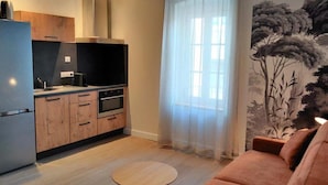 Eine moderne Küche mit Holzschränken, einem eingebauten Ofen und einer schwarzen Arbeitsplatte. Im Wohnbereich steht ein runder Holztisch mit einer Couch.