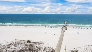 A beach with a concrete walkway leading to the water, beach umbrellas, and a clear view of the ocean.