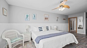 Une chambre à coucher avec un grand lit, des murs blancs et un ventilateur de plafond.