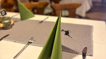 Una mesa de comedor ordenada con un mantel individual, cubiertos y una servilleta verde doblada en forma de cono.