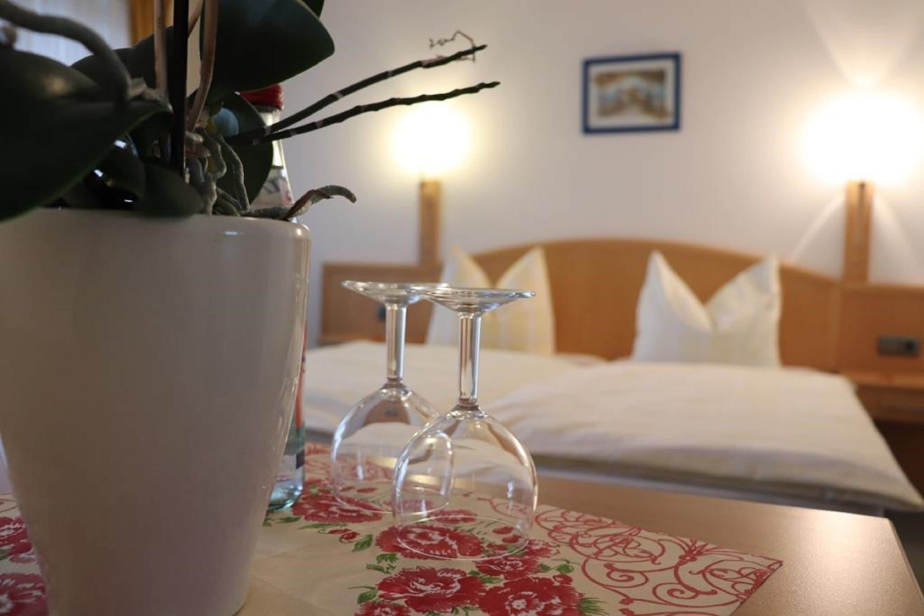 Et hotelværelse med en seng, et natbord med en vase blomster, og to vinglas.