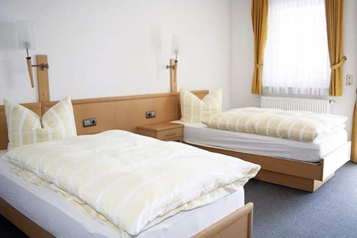 A hotel room with two beds, a nightstand, and a window with curtains.