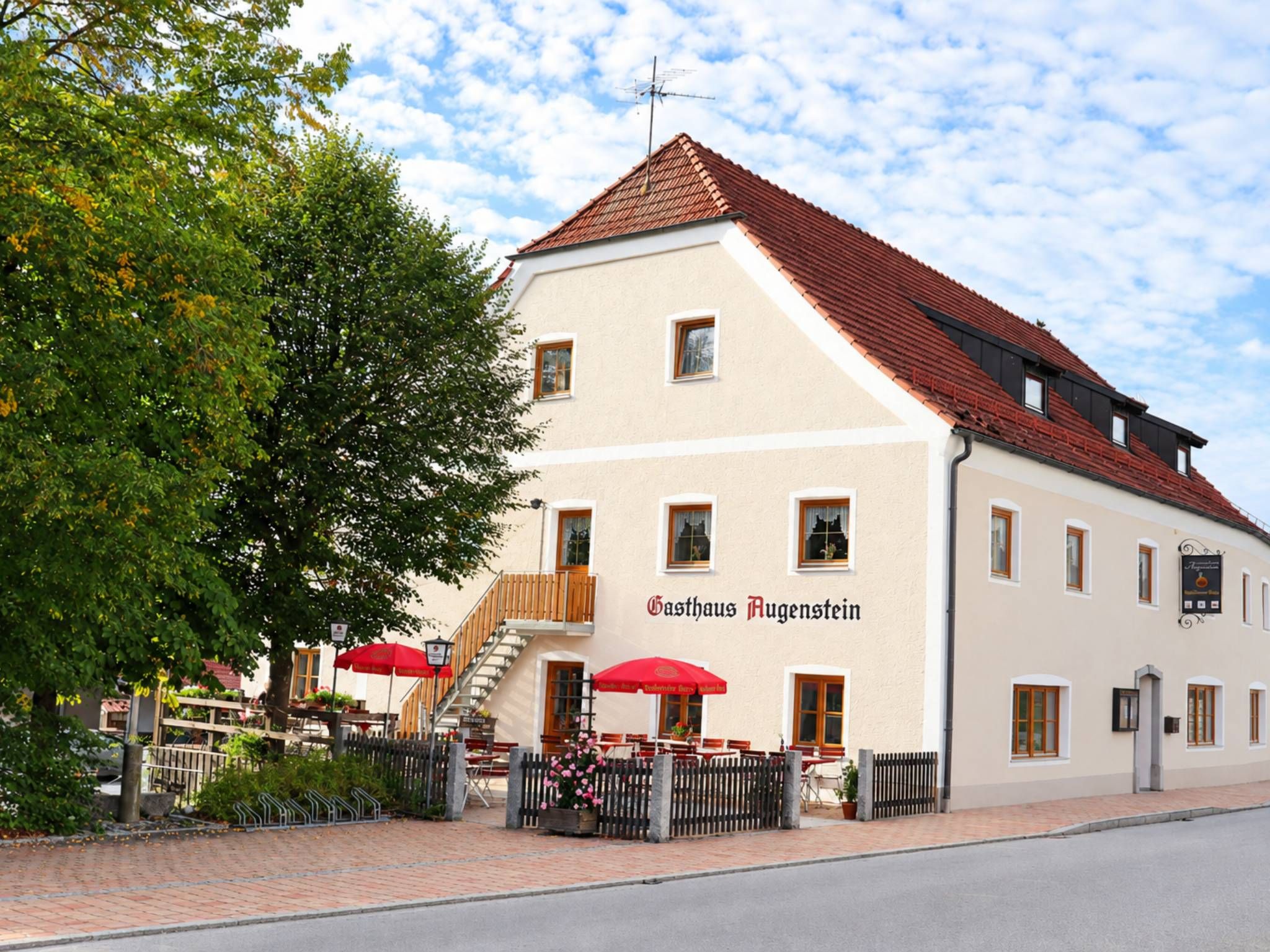 Ein Gebäude mit einem Schild, auf dem 'Gasthaus Aigenstein' steht, und einem roten Sonnenschirm davor.