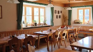 A cozy restaurant with wooden furniture, large windows with curtains, and a variety of plants on the windowsill. - Gasthaus Pension Augenstein (Winzer)