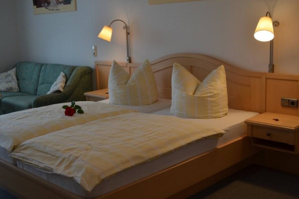 A double bed with a wooden headboard, two bedside lamps, a green armchair, and a bedside table with a lamp.
