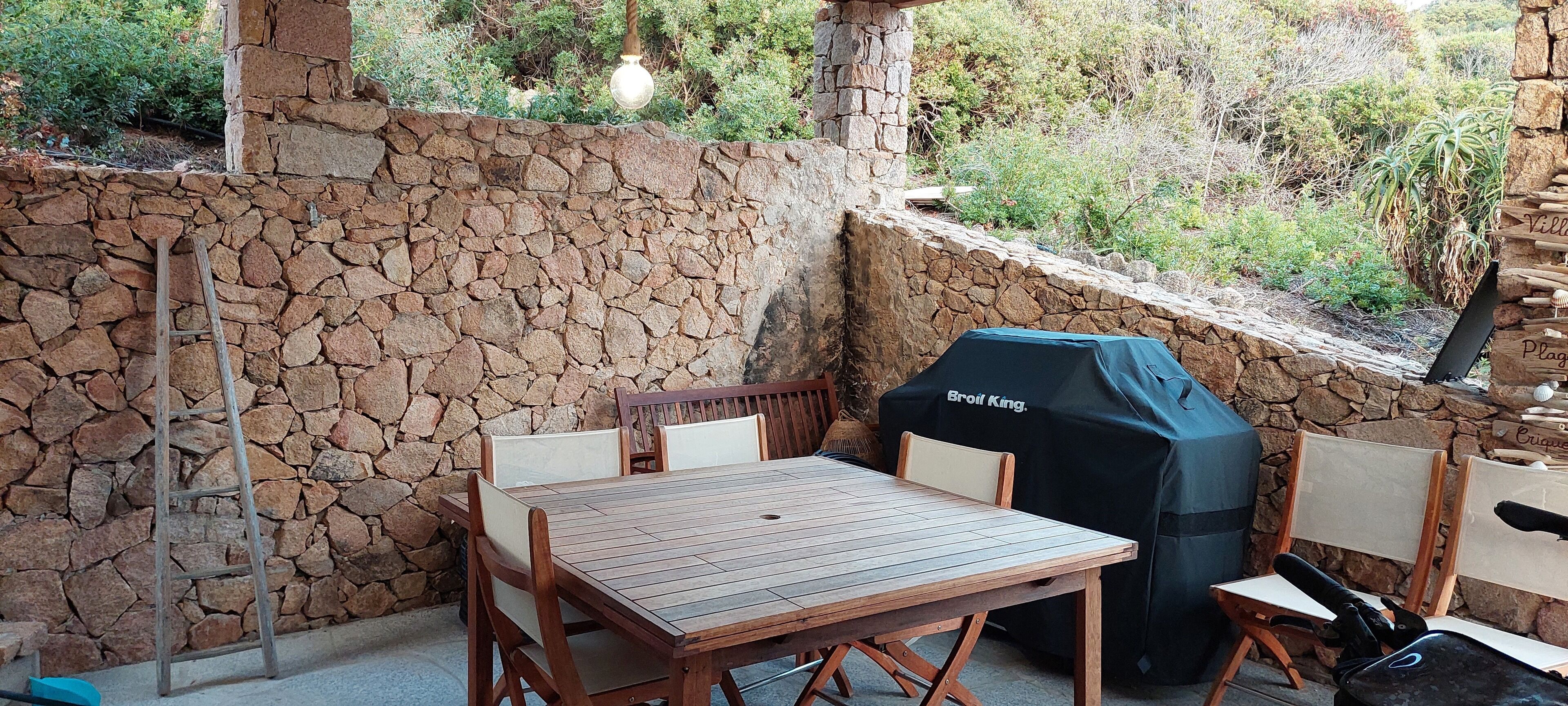 A stone wall with a wooden table and chairs, a grill, and a ladder.