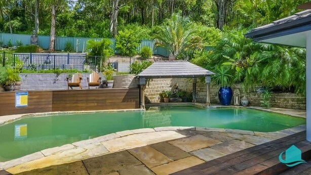 A backyard with a swimming pool, stone deck, and a covered seating area with chairs. - Splendour Hideaway - Luxury and pool - Caves Beach (Caves Beach)