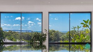 A room with large windows offering a view of a lush landscape and a body of water. - Splendour Hideaway - Luxury and pool - Caves Beach (Caves Beach)