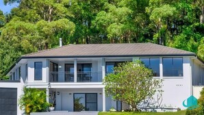 A two-story house with a balcony on the upper floor, surrounded by lush greenery. - Splendour Hideaway - Luxury and pool - Caves Beach (Caves Beach)