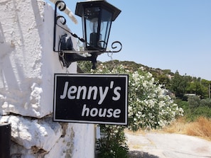 Een bord met de tekst 'Jenny's house' bevestigd aan een witte muur, met een zwarte lantaarn erboven.