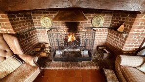 A brick fireplace with a fire, surrounded by leather armchairs and a patterned ottoman. - A Unique Tudor Manor House dating from 1547 (Painters Forstal)