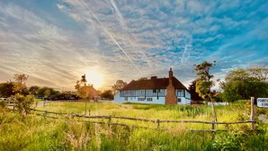 A traditional Tudor-style house with a thatched roof, surrounded by a grassy field and a wooden fence. - A Unique Tudor Manor House dating from 1547 (Painters Forstal)
