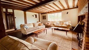 A cozy living room with a high ceiling, wooden beams, and a fireplace. There are two sofas and a coffee table. - A Unique Tudor Manor House dating from 1547 (Painters Forstal)