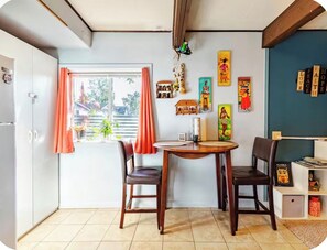 Uma área de refeições com mesa redonda, duas cadeiras, janela com cortinas e decorações nas paredes.