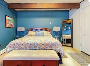 A bedroom with a bed, two bedside lamps, a wooden headboard, a bench, and a door leading to a bathroom.