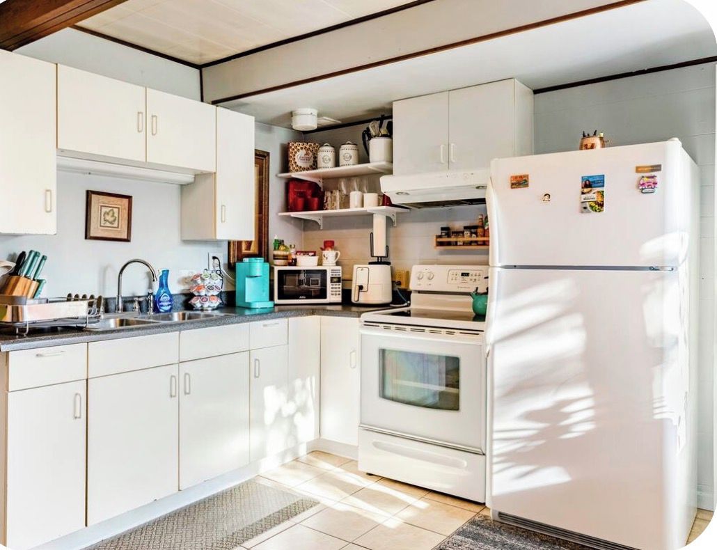 Una cocina con armarios blancos, estufa, microondas y refrigerador.