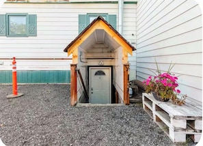 A small wooden structure with a door, possibly a guest entryway, next to a white building with green shutters.