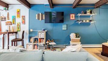 Una habitación con pared azul, un televisor de pantalla plana montado sobre una estantería, un sofá con cojines estampados y techo de madera.