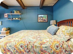 A bedroom with a bed, a lamp, a shelf with items, and a framed picture on the wall. - Large Govt hill studio-near  downtown (Anchorage)