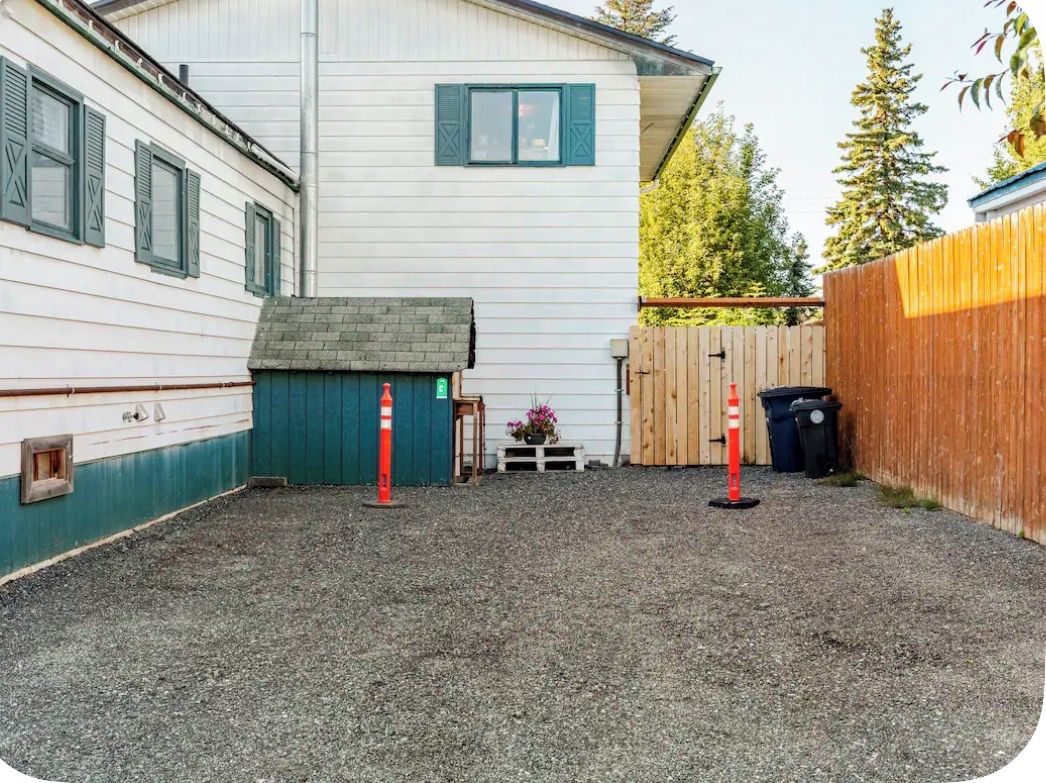 A residential property with a gravel driveway, a wooden fence, and a white building with green shutters.