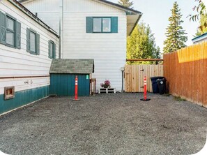 A residential property with a gravel driveway, a wooden fence, and a white building with green shutters.