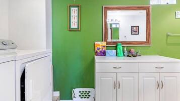 Uma lavanderia com máquina de lavar, um armário branco e uma parede verde.