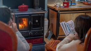 A room with a wood-burning stove, a table with a kettle, and a person reading a book. - Cottage 70m² for 2p - Regional Park of Haut-Languedoc-calm-nature (Cambounès)