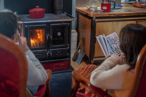 Une pièce avec un poêle à bois, une table avec une bouilloire et une personne qui lit un livre.