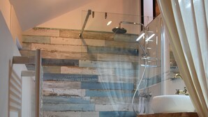 Ein Badezimmer mit Holzboden, einer Duschkabine mit Glastür, einem Waschbecken und einem Holzregal.