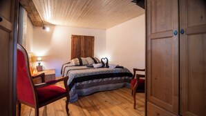 A bedroom with a wooden floor, a bed with patterned bedding, a red chair, a wooden wardrobe, and a nightstand with a lamp. - Cottage 70m² for 2p - Regional Park of Haut-Languedoc-calm-nature (Cambounès)
