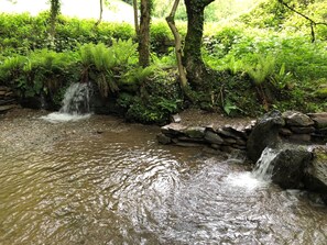 Une petite cascade se trouve dans une zone boisée luxuriante et verdoyante, avec un mur de pierre et un ruisseau aux eaux claires.
