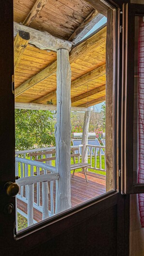 Une terrasse en bois avec une balustrade blanche, un banc et une vue sur la verdure et des fleurs roses.