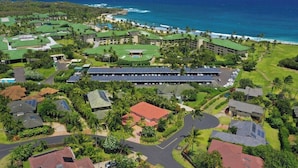 An aerial view of a resort with multiple buildings, a parking area, and a view of the ocean.