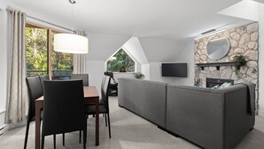 A modern living room with a dining area, stone wall, fireplace, and a flat-screen TV.
