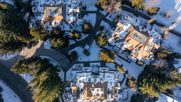 An aerial view of a residential area with multiple houses, surrounded by trees and covered in snow.